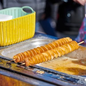 Cooked spiral fried potato, rich in fat and calories fast food, unhealthy but very delicious dish on street food festival. Close up spiral potato tornado cooked in fryer
